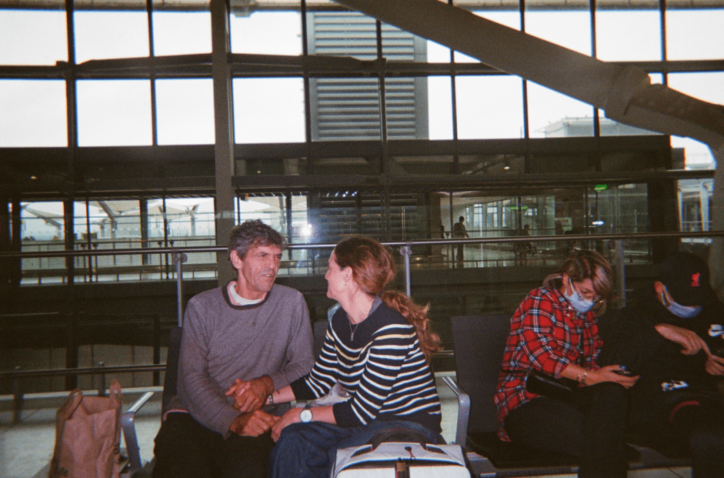 A man and a woman sitting together on an airport bench.