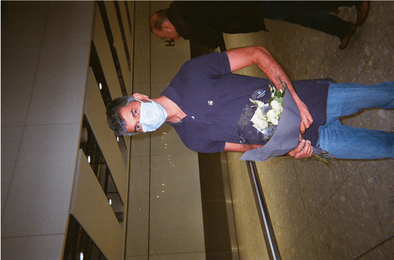 A man in a mask holding a bouquet of white flowers.